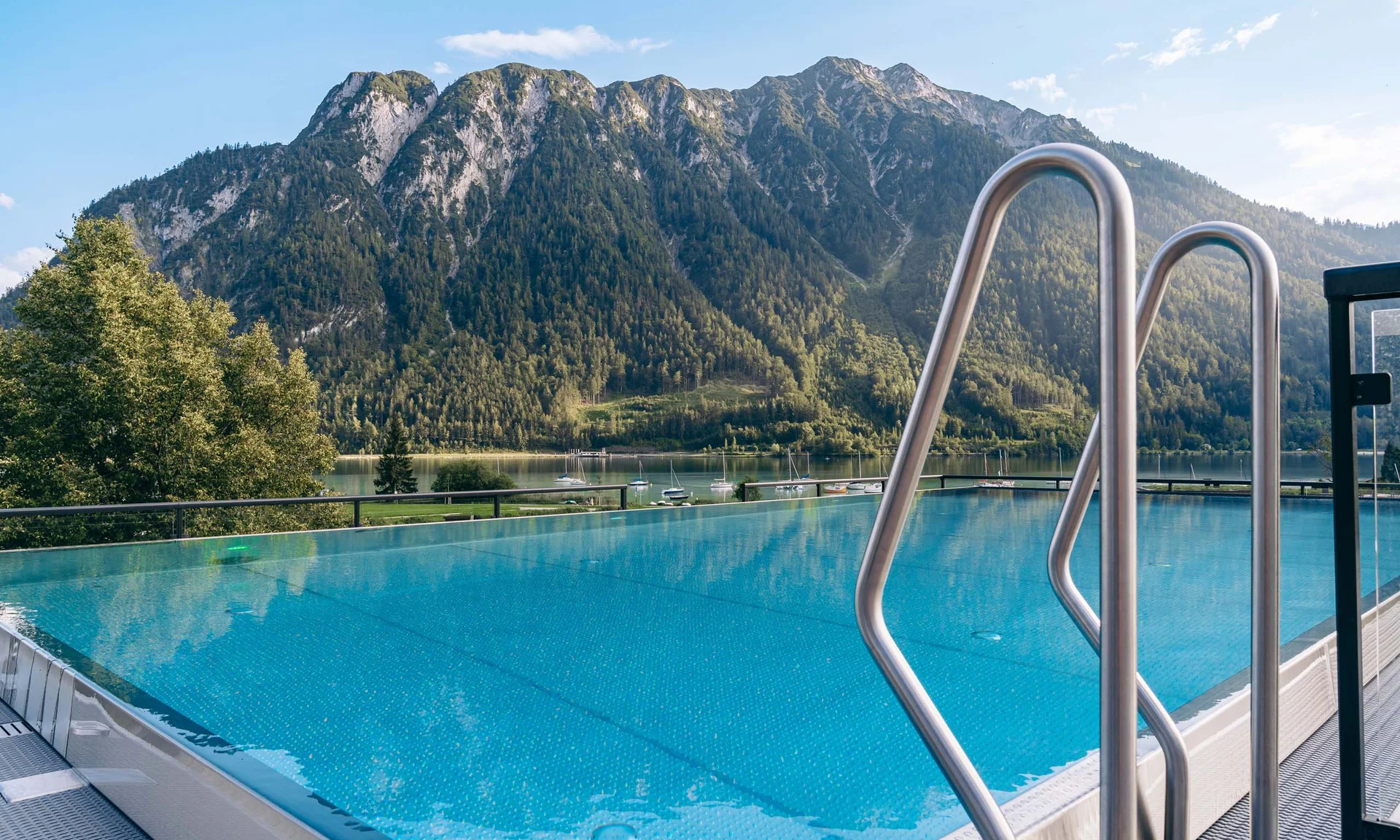 Infinity-Pool mit Bergblick und See im Hintergrund bei sonnigem Wetter