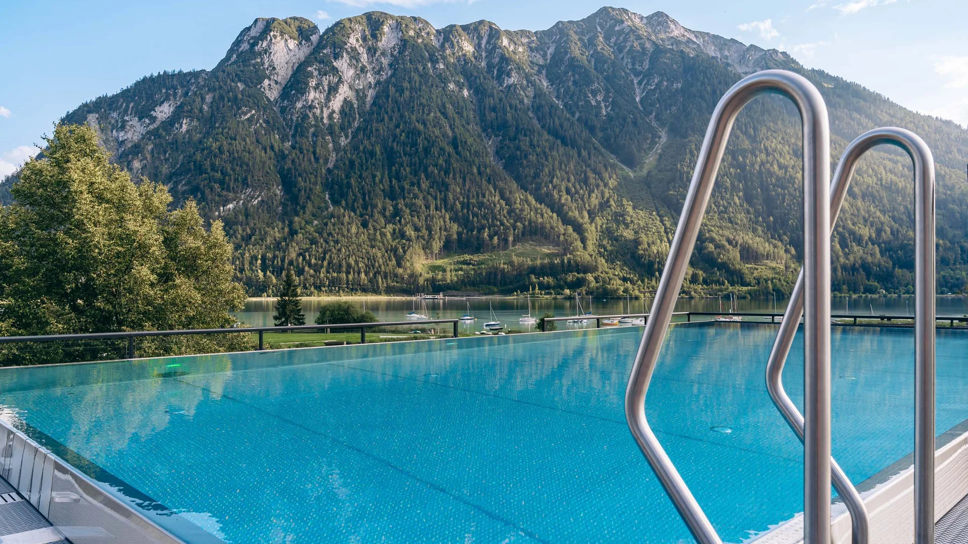 Infinity-Pool mit Bergblick und See im Hintergrund bei sonnigem Wetter
