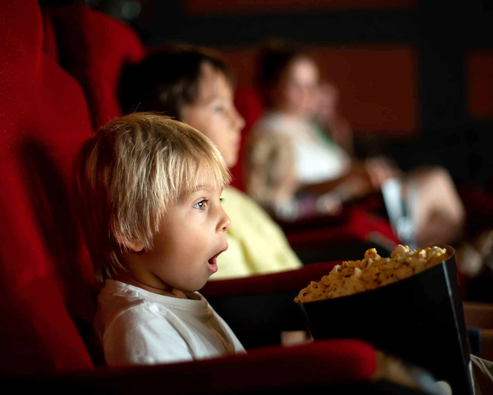 Kind schaut überrascht im Kino sitzend mit Popcorn