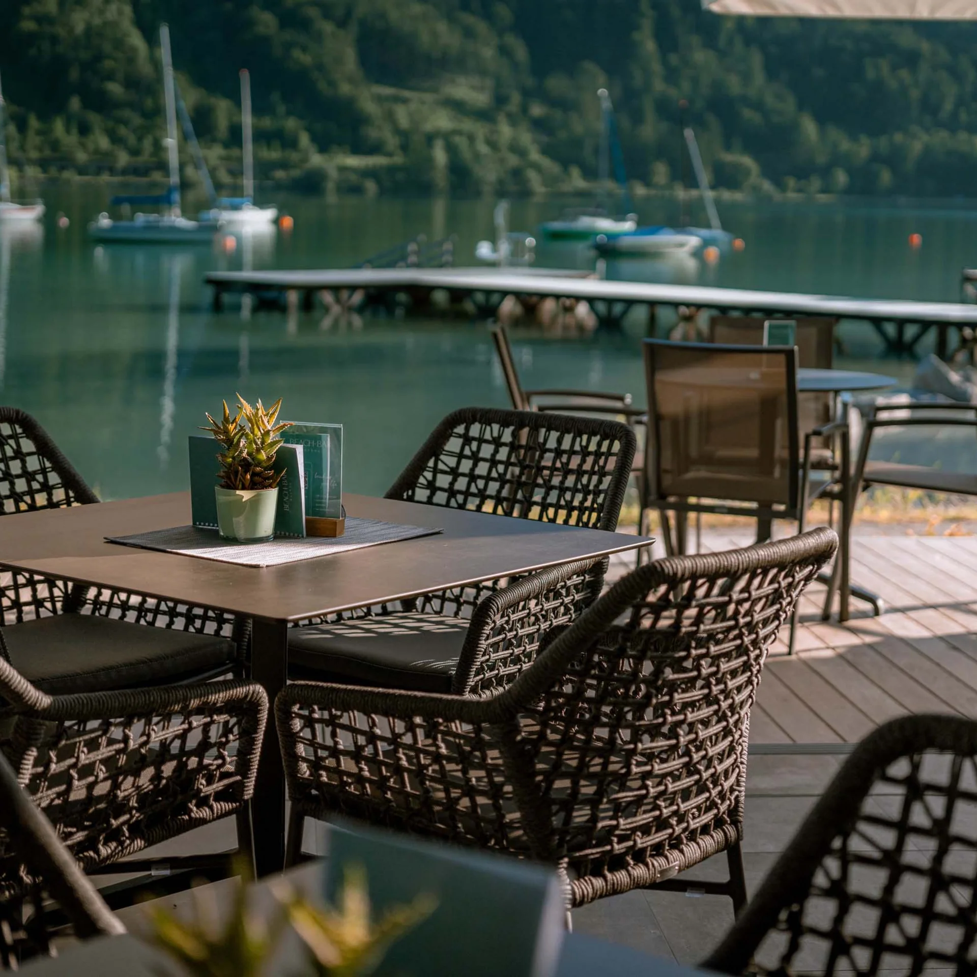 Empty seating at a terrace table overlooking a lake and dock
