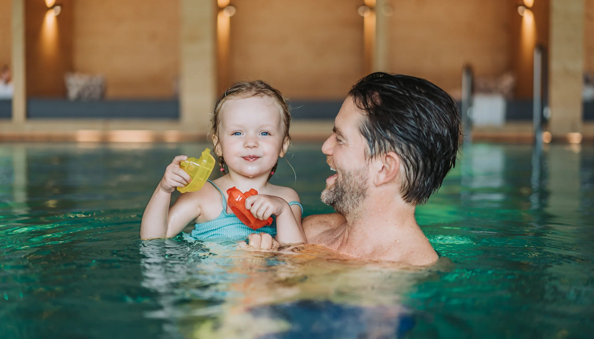 Vater hält lachendes kleines Mädchen mit Spielzeugbooten im Hallenbad