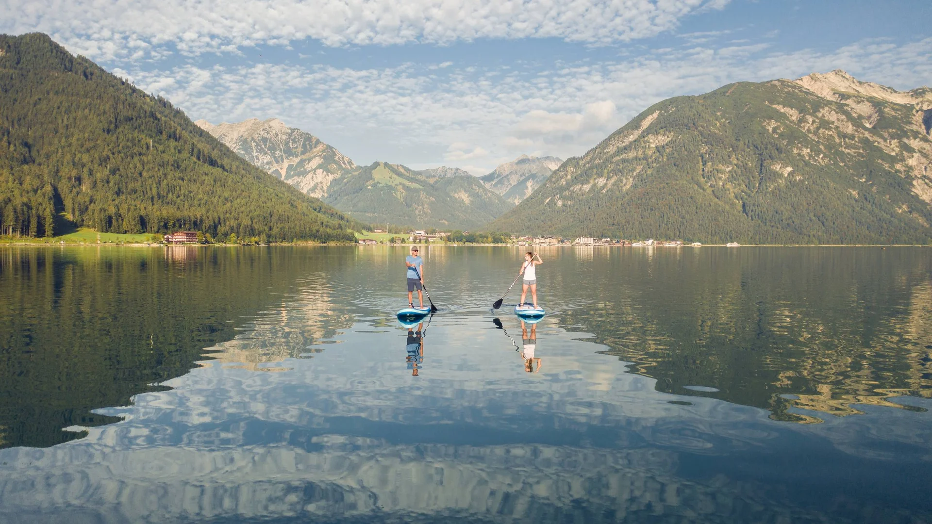 Zwei Menschen beim Stand-up-Paddling auf einem Bergsee mit bewölktem Himmel