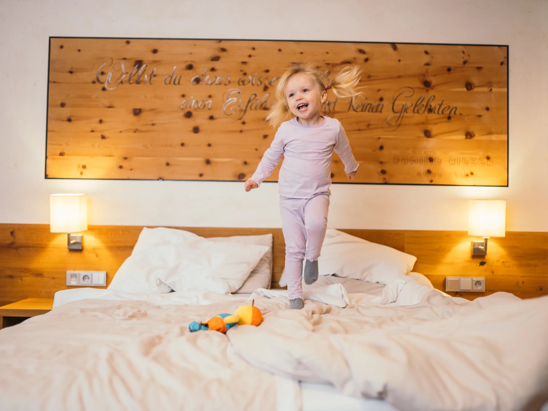 Kleines Mädchen springt lachend im Pyjama auf einem Bett im Schlafzimmer