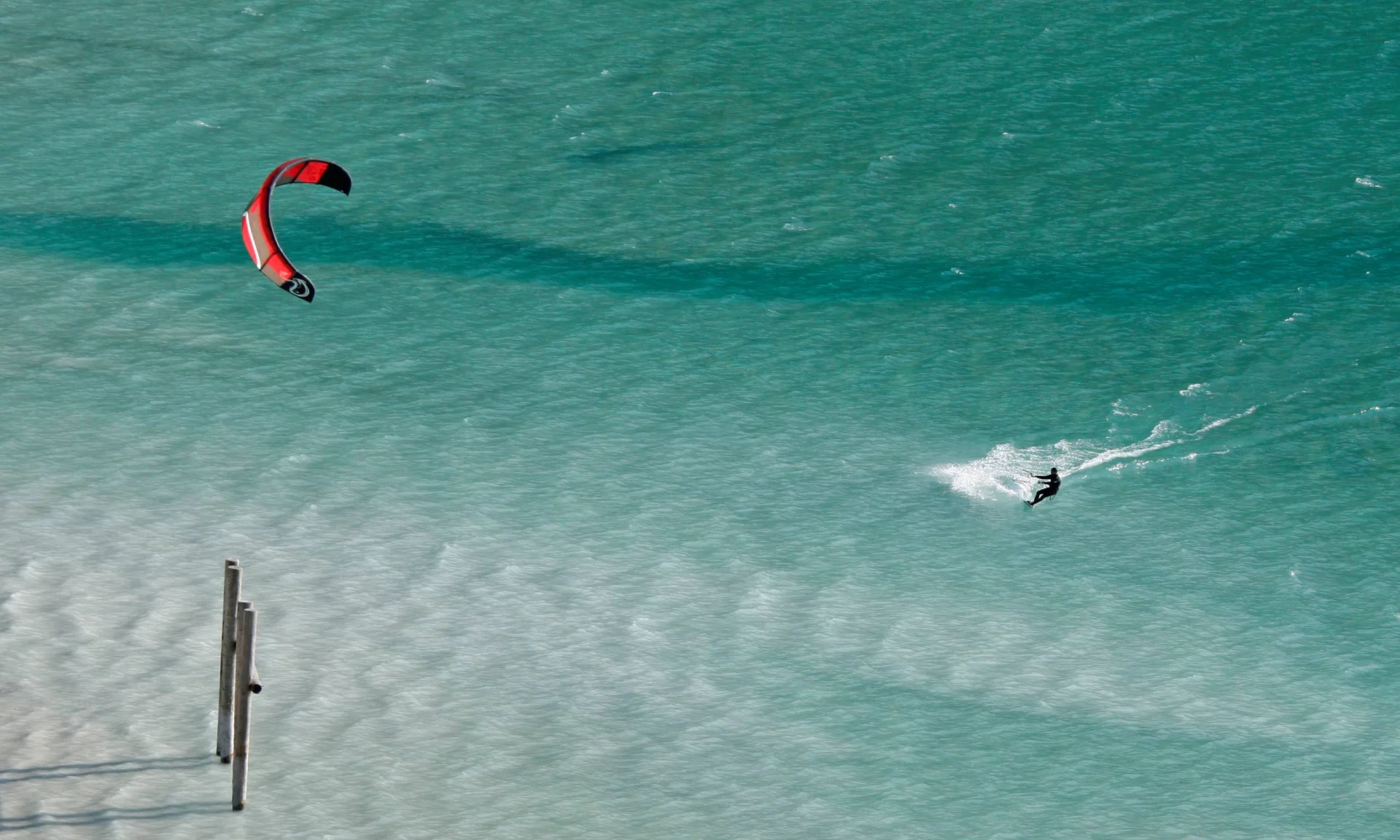 Kitesurfer mit rotem Kite auf türkisfarbenem Wasser bei sonnigem Wetter