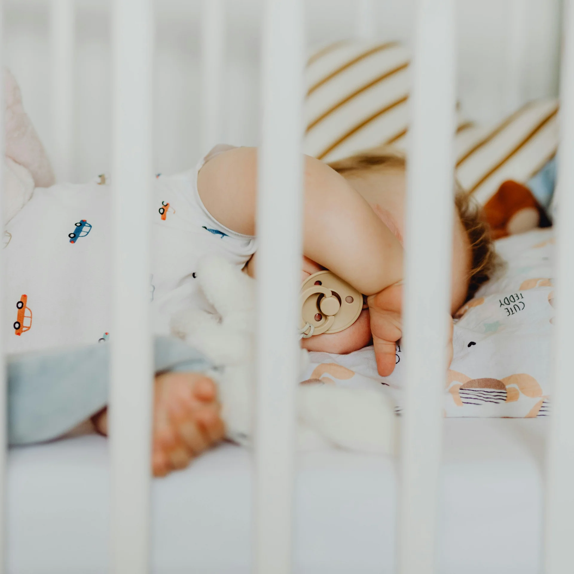 Sleeping baby with pacifier in a crib with white bars
