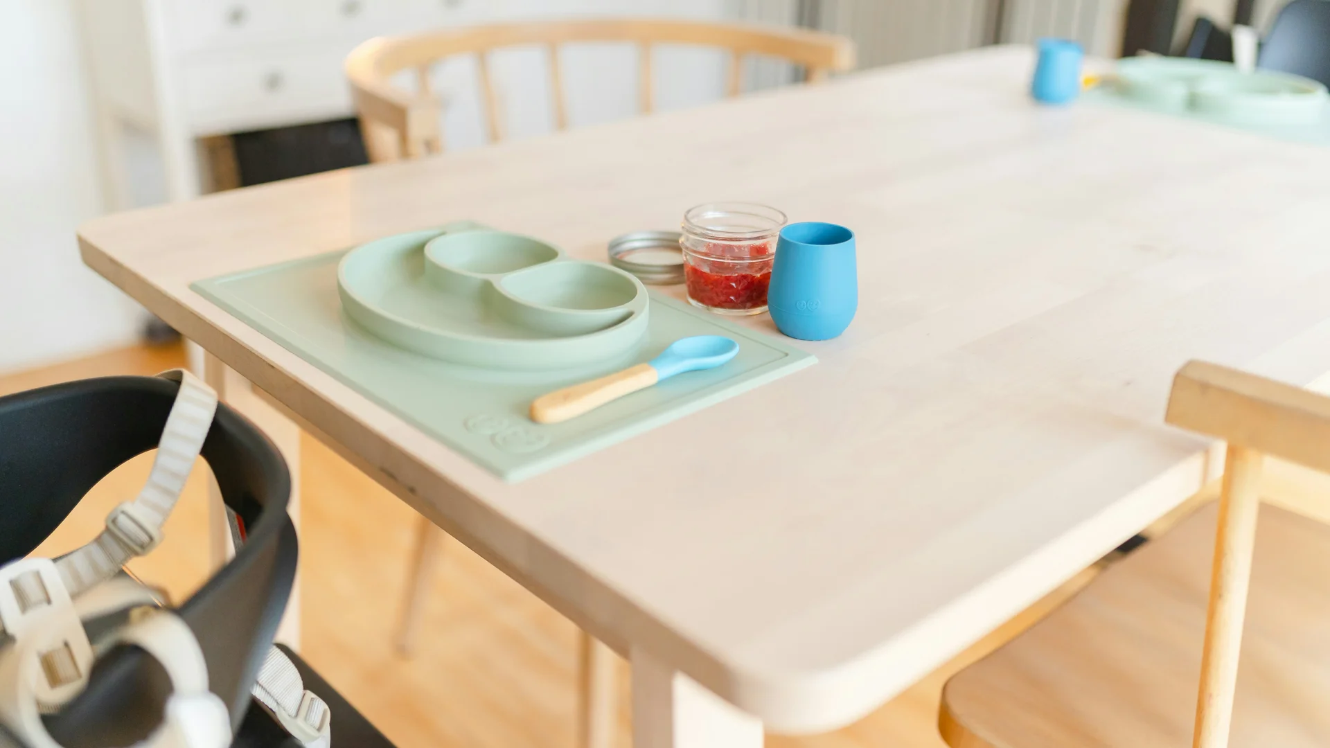 Familienresort Buchau: Ihr Babyhotel in Tirol Kinderhochstuhl an hellem Holztisch mit Babyteller, Löffel und Glas Marmelade