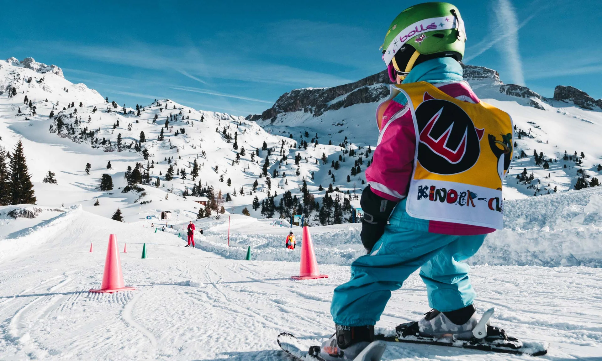 Kind fährt Ski auf verschneiter Piste mit bunten Hütchen und Bergen im Hintergrund