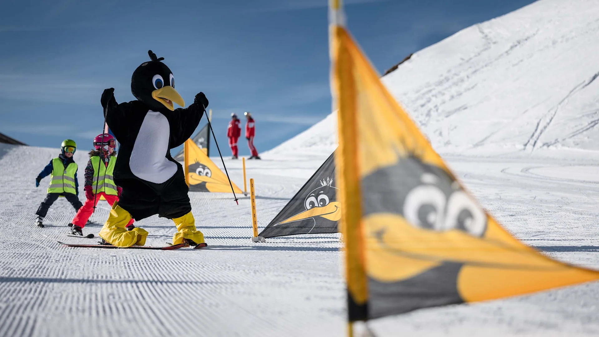 Person im Pinguinkostüm und Kinder beim Skifahren im Schnee