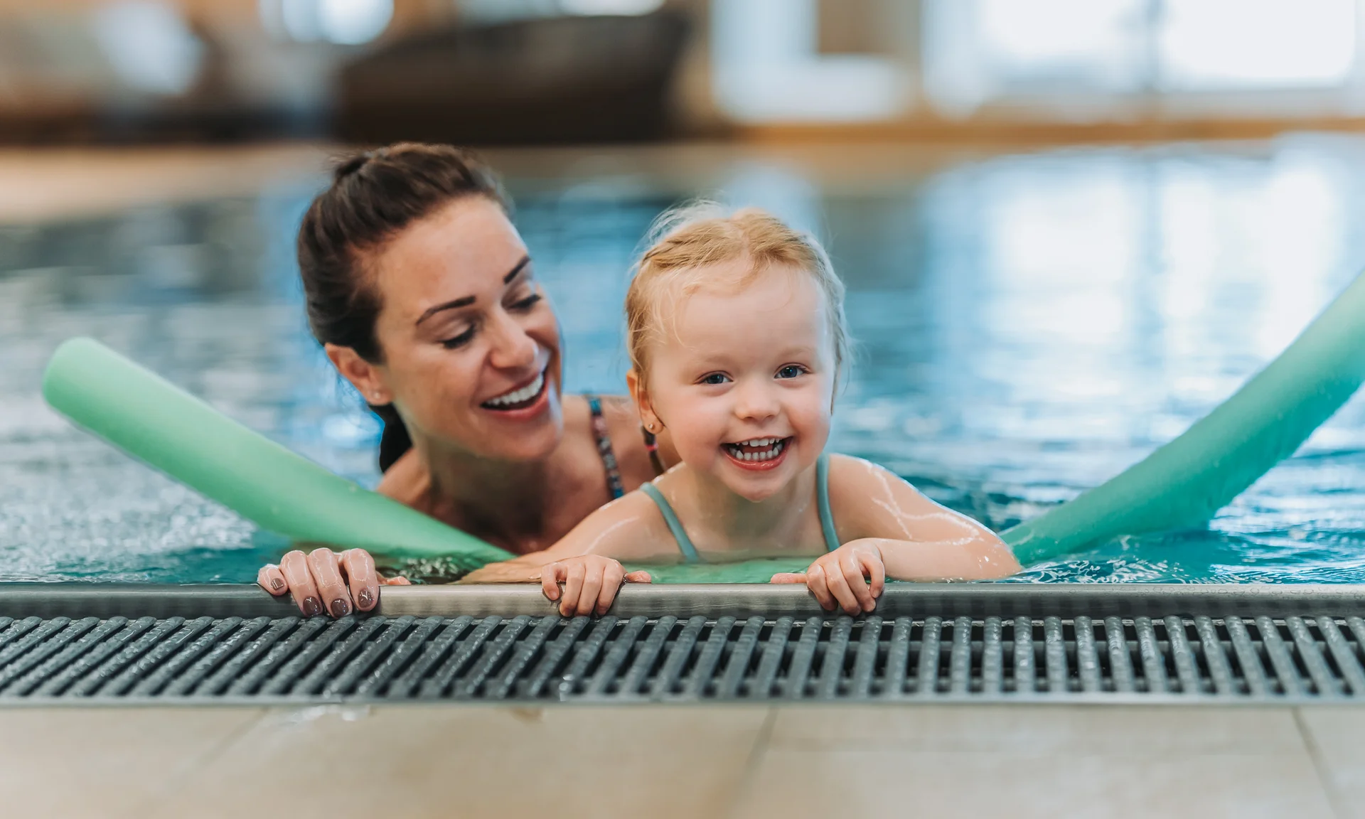 Glückliches Kind mit Schwimmnudeln lernt im Schwimmbad mit Frau schwimmen