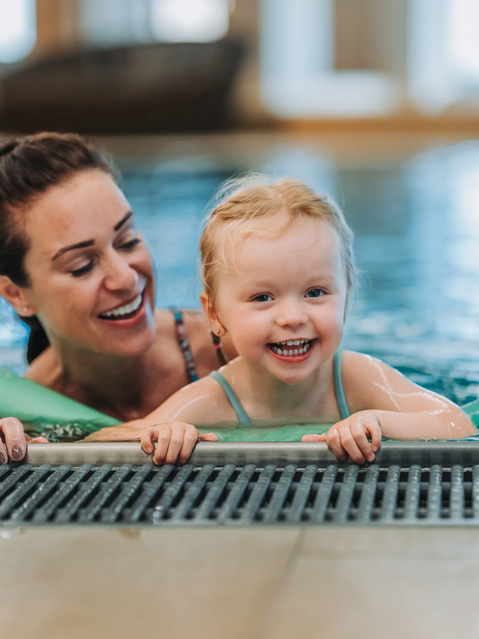 Happy child learning to swim with foam noodles in a pool with a woman