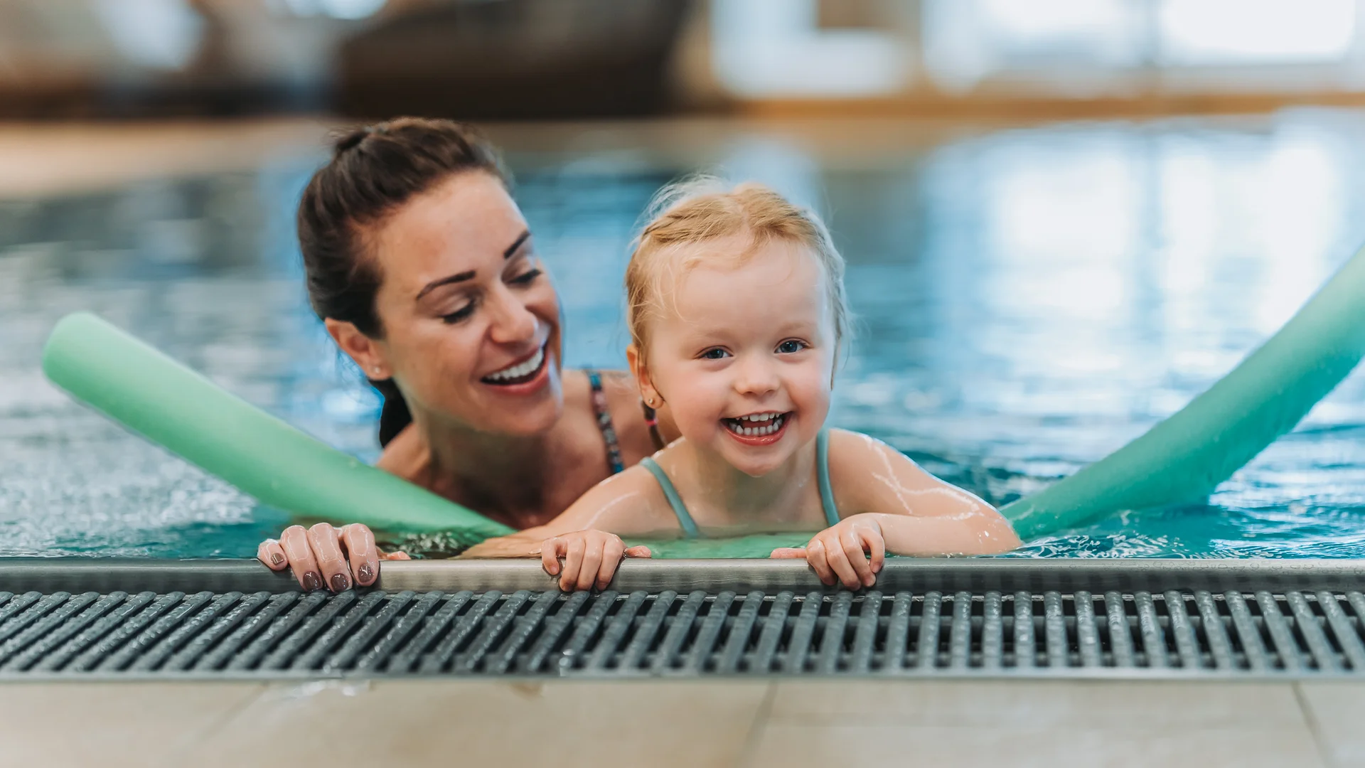 Glückliches Kind mit Schwimmnudeln lernt im Schwimmbad mit Frau schwimmen