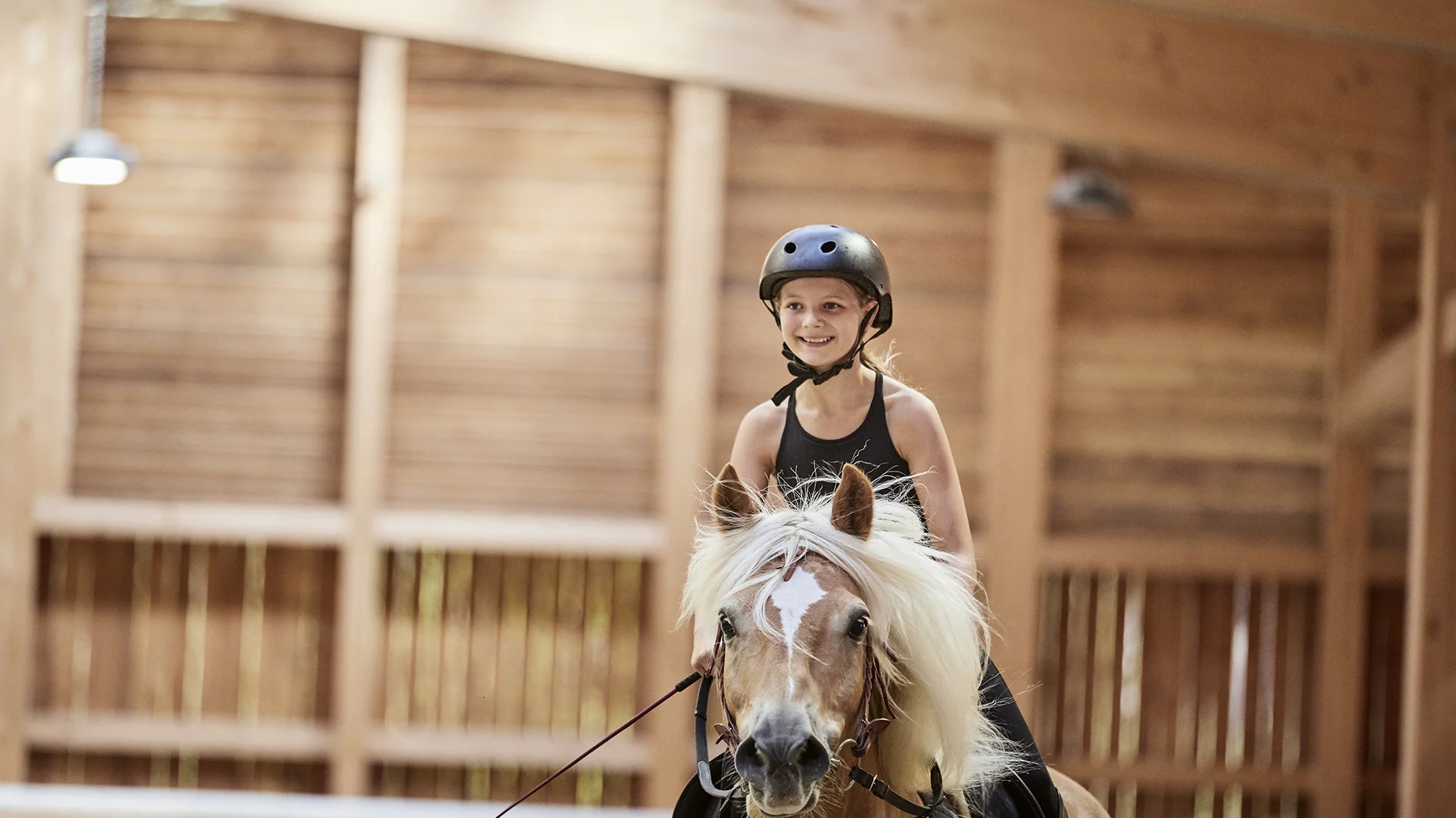 Lächelndes Mädchen reitet Pony in einer Reithalle mit Helm