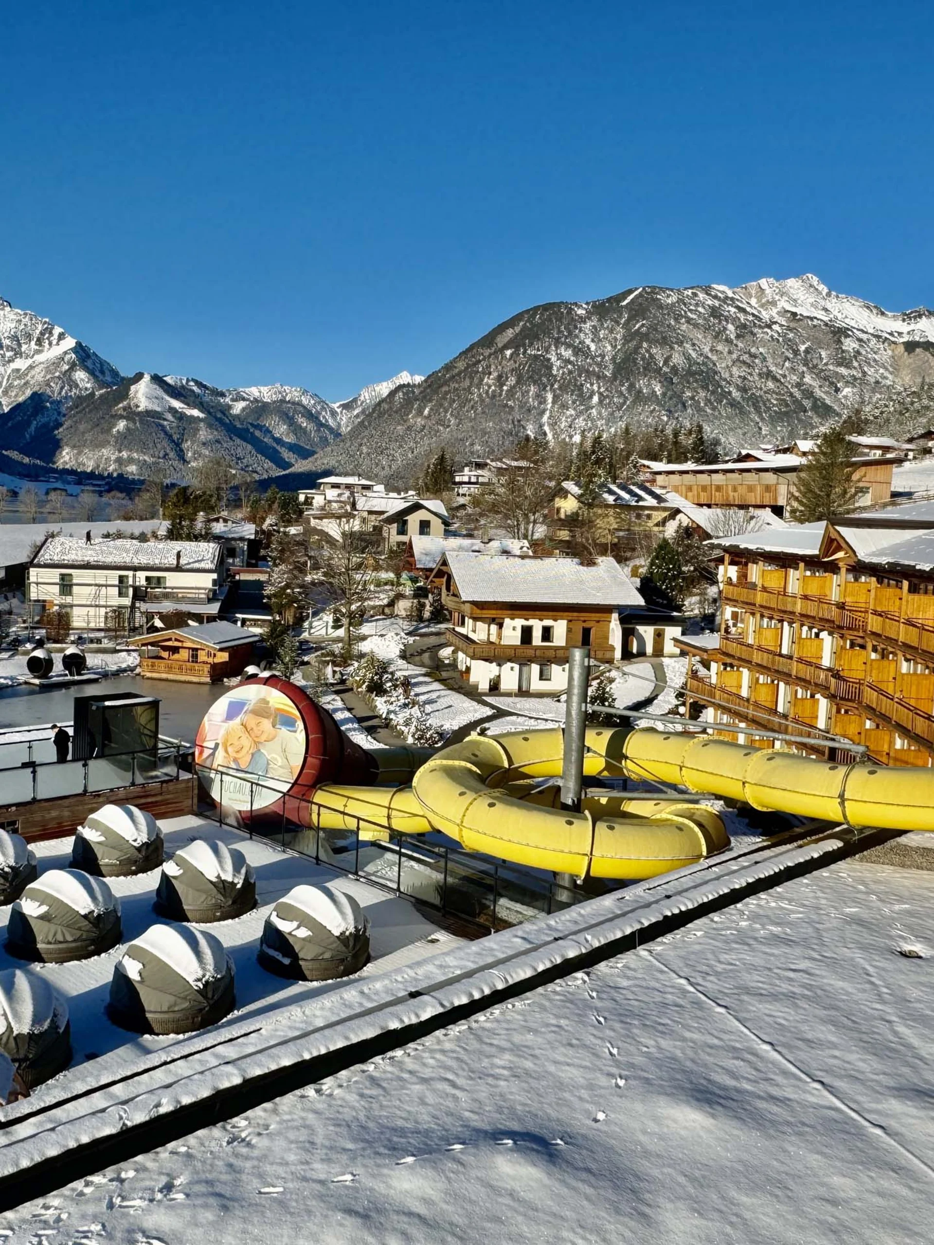 Winterlandschaft mit verschneitem Resort, Wasserrutsche und Bergen im Hintergrund