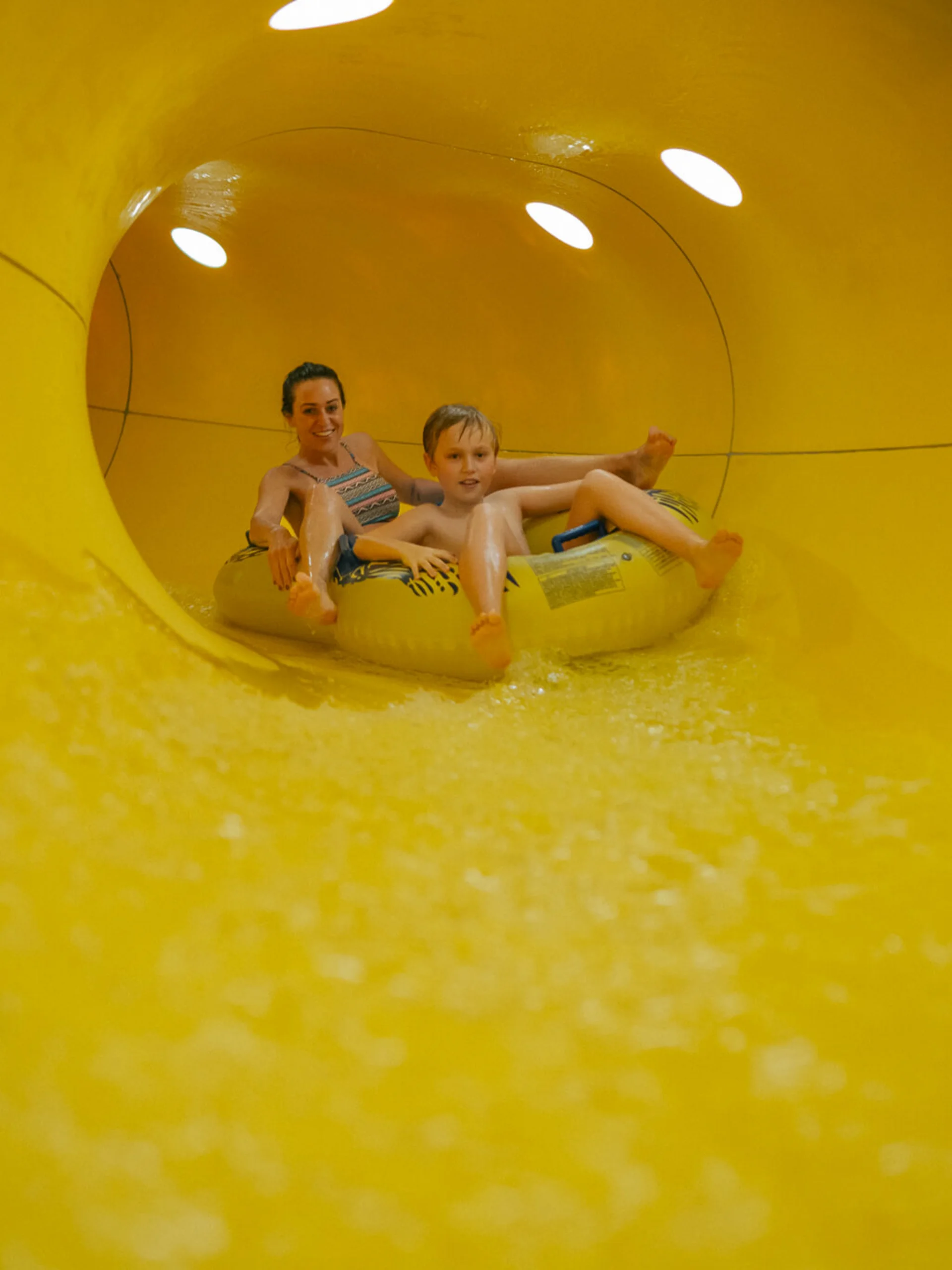 Mutter und Sohn fahren gemeinsam auf einem Schlauchreifen in einer gelben Wasserrutsche