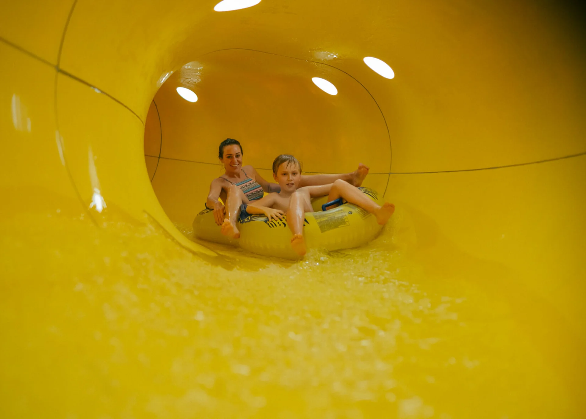 Mutter und Sohn fahren gemeinsam auf einem Schlauchreifen in einer gelben Wasserrutsche