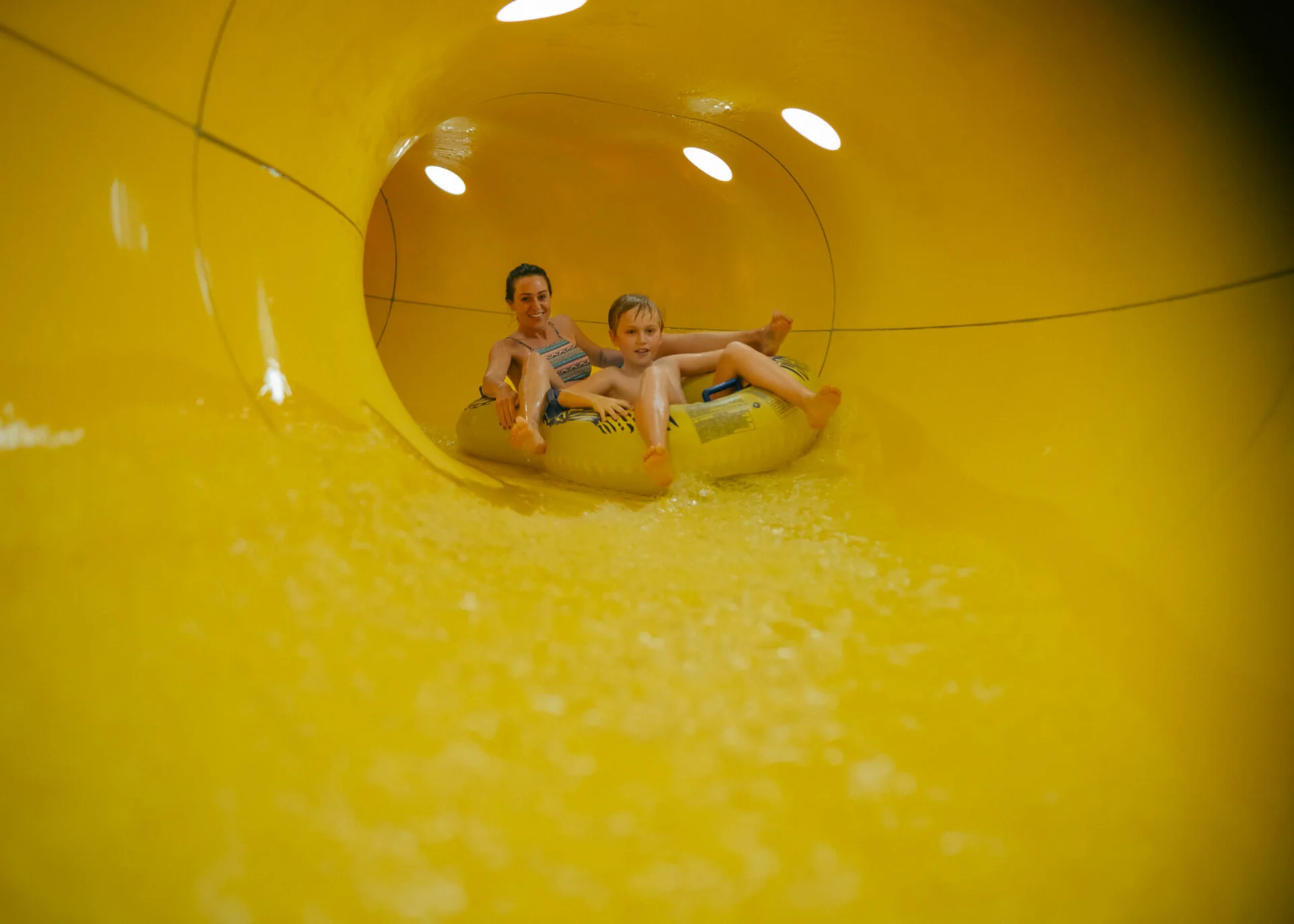 Mutter und Sohn fahren gemeinsam auf einem Schlauchreifen in einer gelben Wasserrutsche