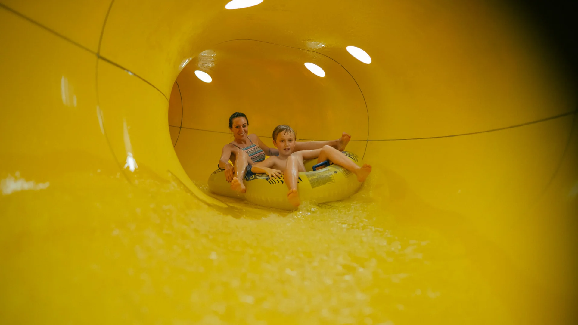 Mutter und Sohn fahren gemeinsam auf einem Schlauchreifen in einer gelben Wasserrutsche