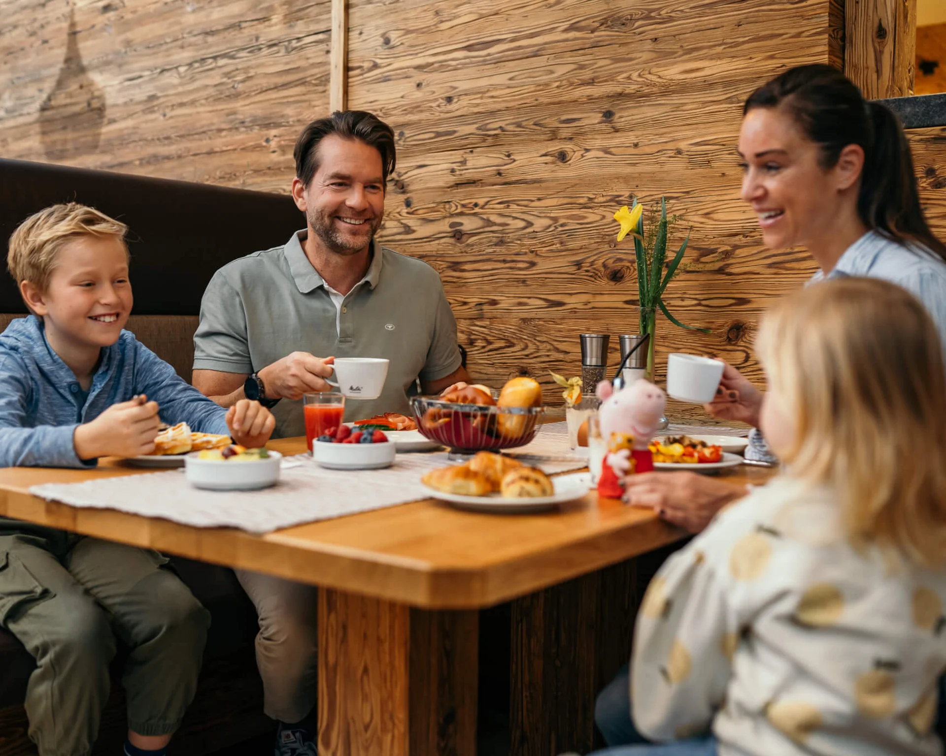 Familie mit zwei Kindern isst Frühstück an Holztisch in gemütlichem Restaurant