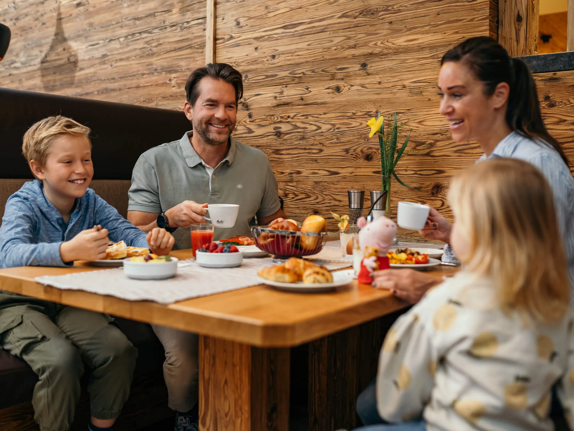 Familie mit zwei Kindern isst Frühstück an Holztisch in gemütlichem Restaurant