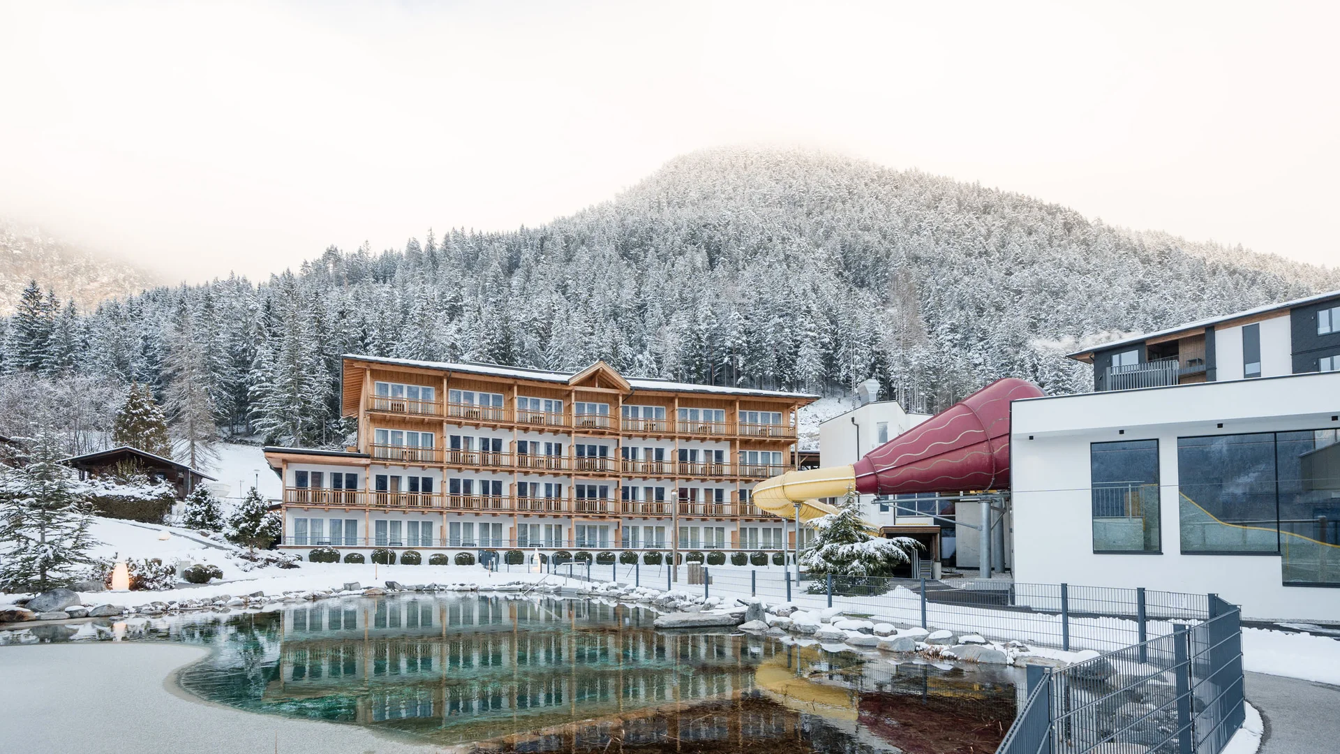 Hotel mit Rutsche und Teich vor verschneitem Berg im Winter