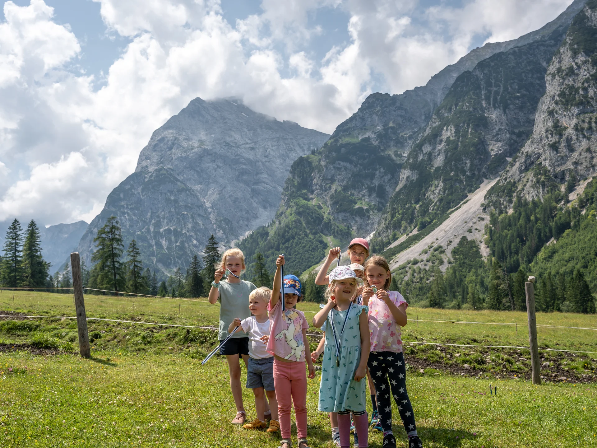Sieben Kinder zeigen im Bergwiesenfeld Auszeichnungen vor beeindruckenden Bergen