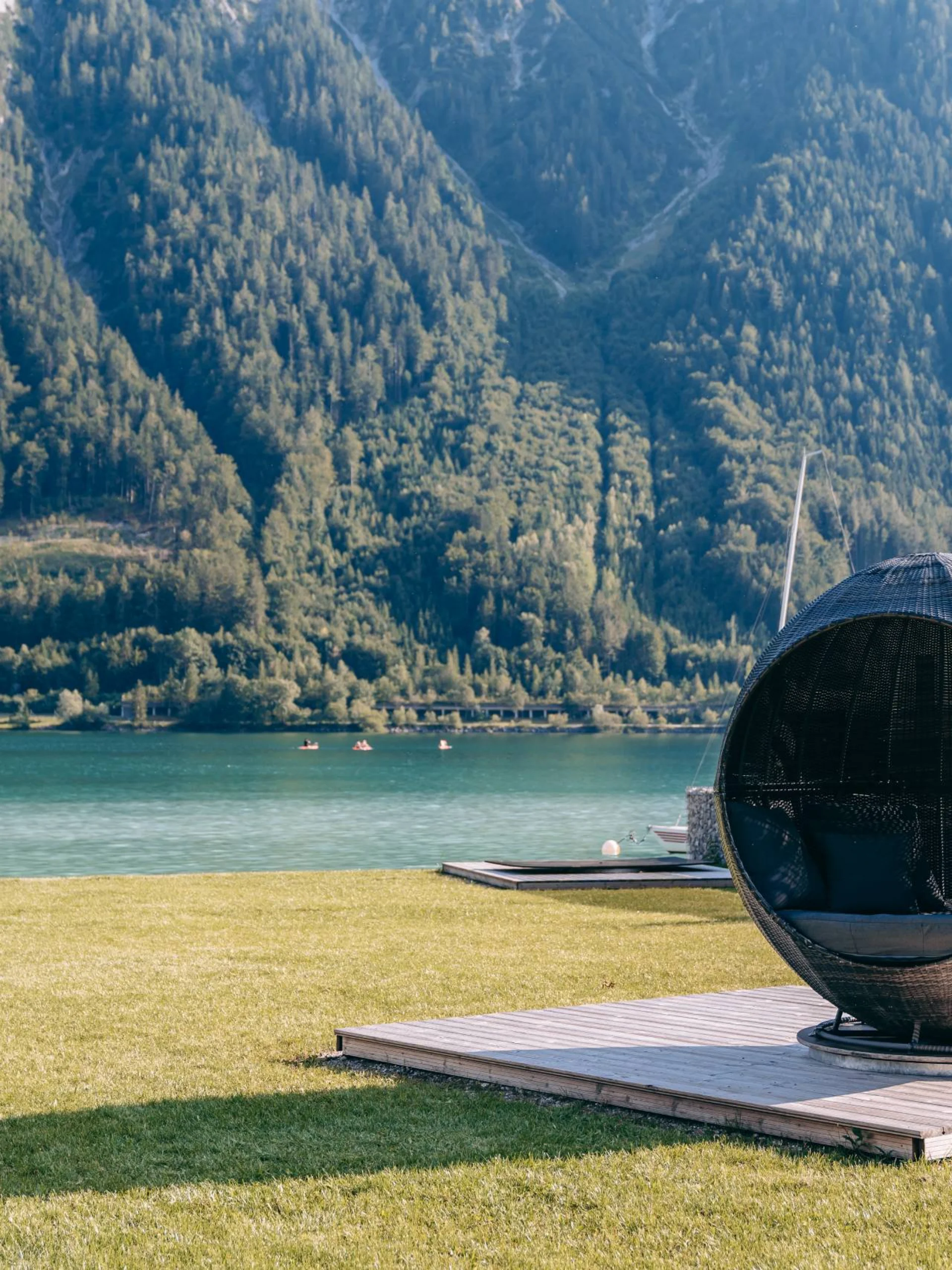 Kugelsessel auf Holzplattform mit Bergsee und bewaldeten Bergen im Hintergrund