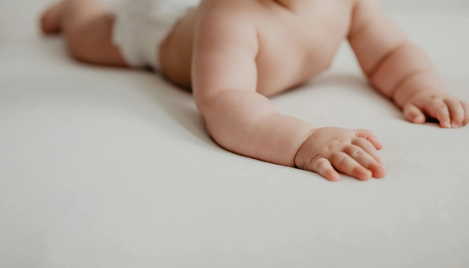 Baby crawling on a white surface, only torso and arms visible