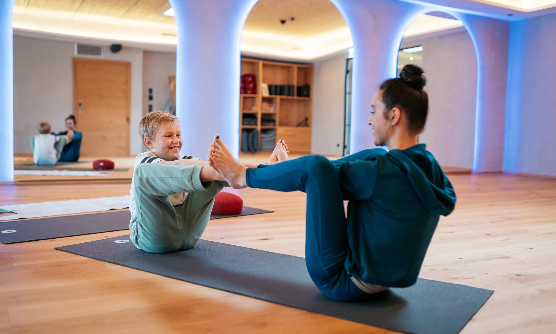 Frau und Kind machen gemeinsam Yogaübungen auf Matten in einem Raum
