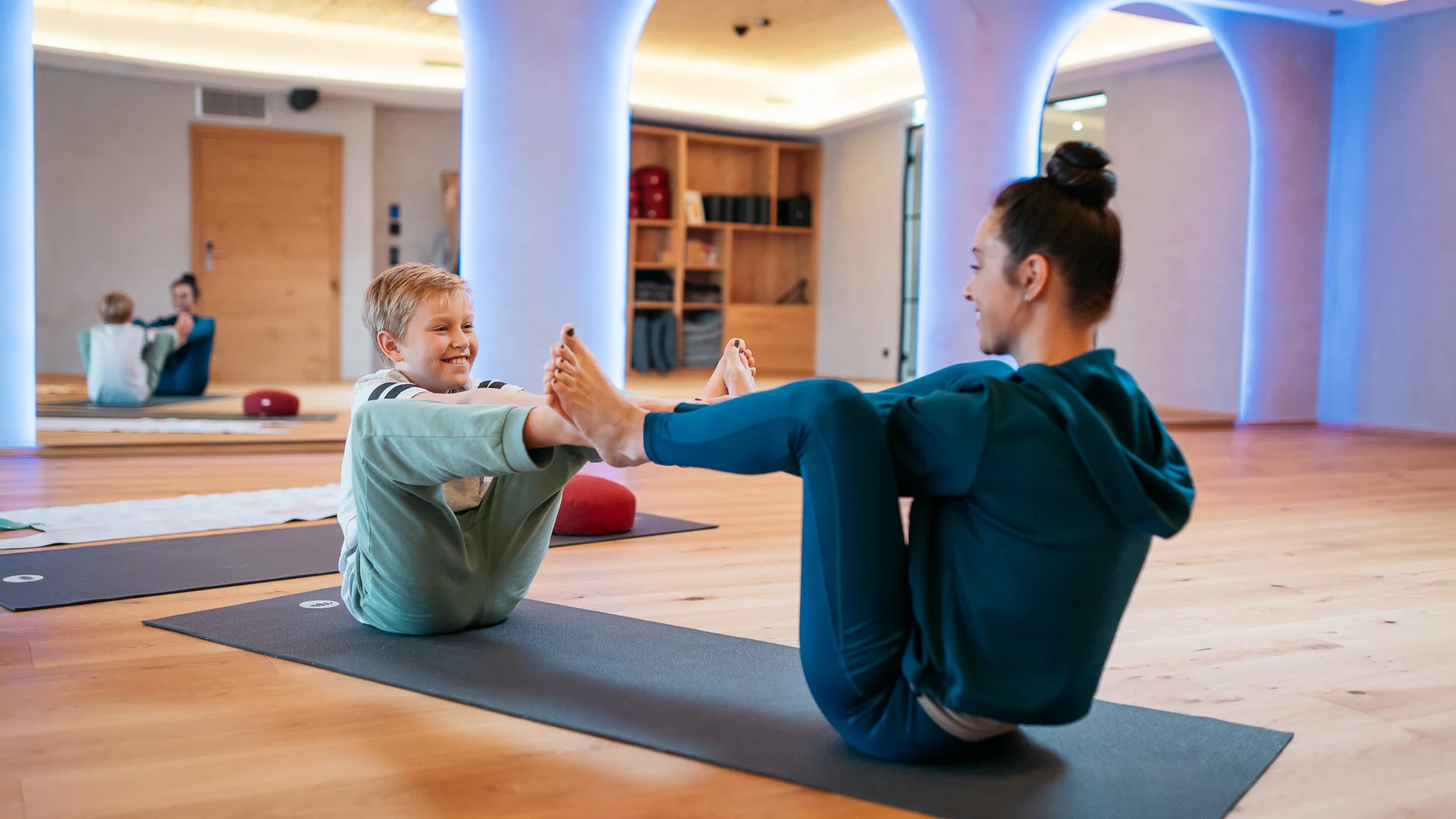 Frau und Kind machen gemeinsam Yogaübungen auf Matten in einem Raum