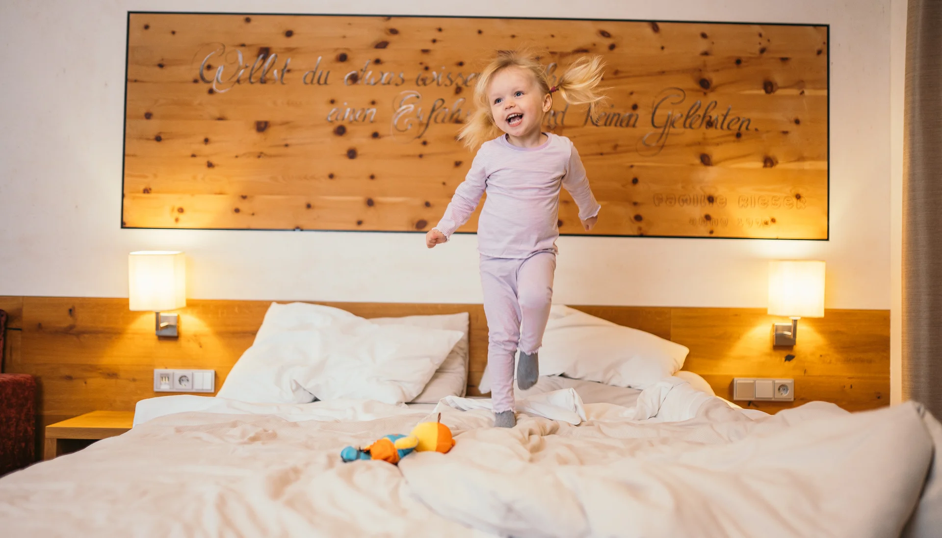 Glückliches kleines Mädchen springt auf einem Bett in einem gemütlichen Schlafzimmer