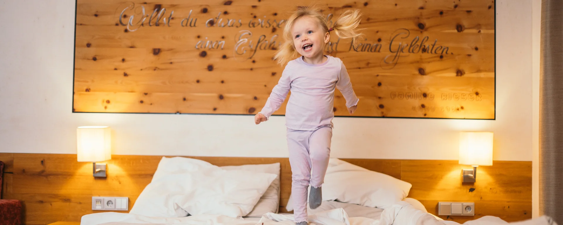 Glückliches kleines Mädchen springt auf einem Bett in einem gemütlichen Schlafzimmer