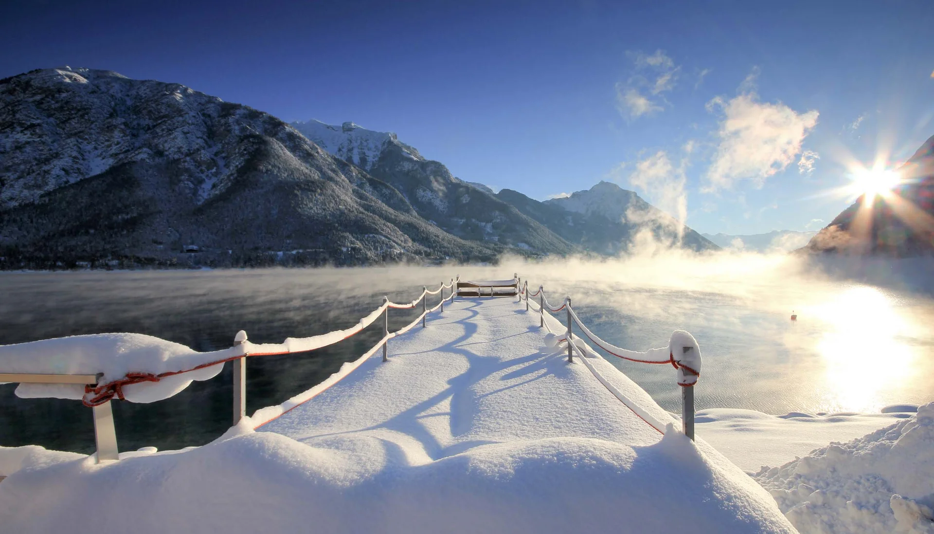 Outdoorspaß im Familienhotel am See in Österreich Verschneiter Steg am See mit Bergen und Sonne im Winter