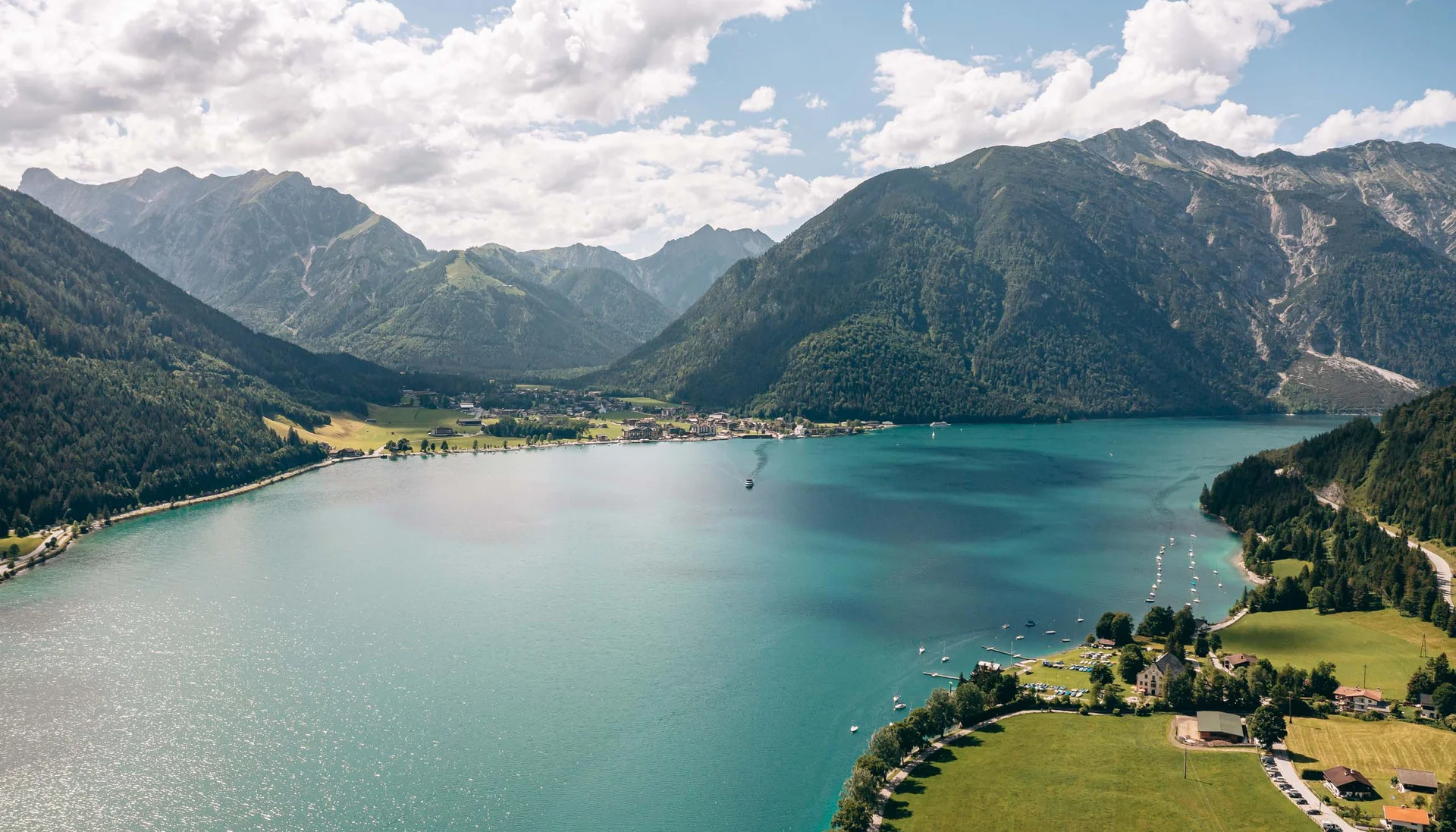 Bergsee mit klaren blauen Wasser, umgeben von grünen Bergen und Dorf am Ufer