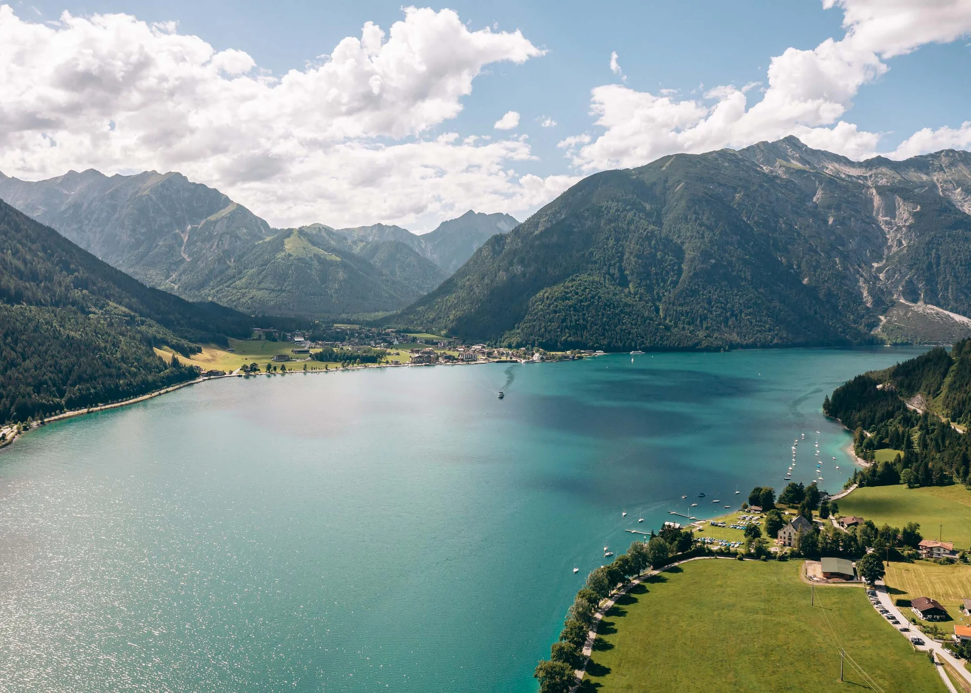 Ihr hundefreundliches Hotel in Tirol am Achensee Bergsee mit klaren blauen Wasser, umgeben von grünen Bergen und Dorf am Ufer