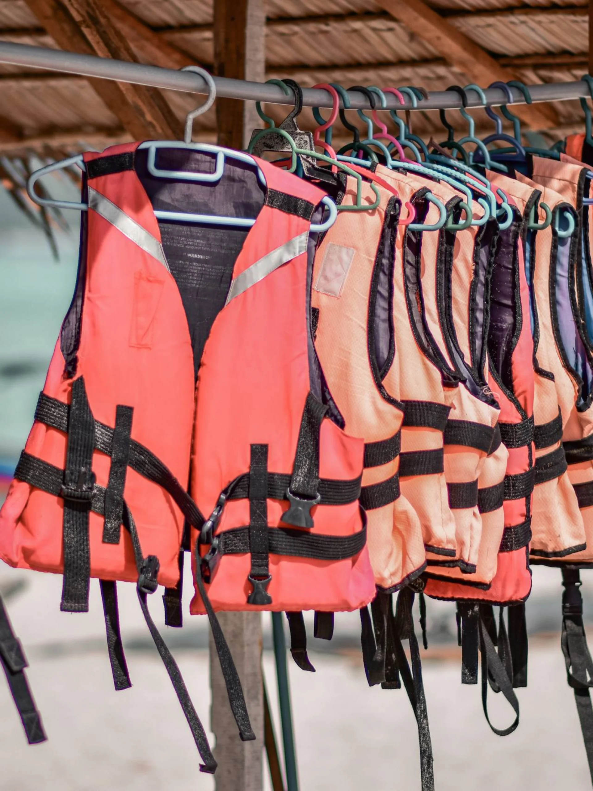 Orange Rettungswesten hängen an einer Stange unter einem Strohdach am Strand