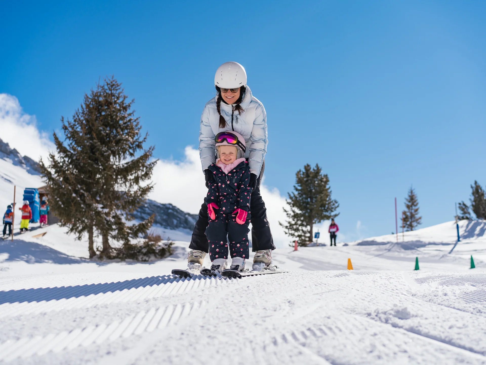 Erwachsene und Kind lernen gemeinsam Skifahren auf verschneiter Piste bei sonnigem Wetter