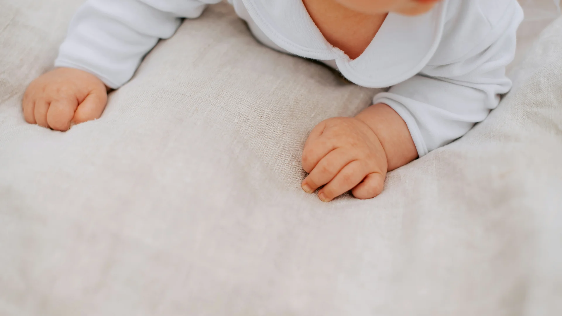 Familienresort Buchau: Ihr Babyhotel in Tirol Nahaufnahme der Hände eines Babys auf einer hellen Decke in weißer Kleidung