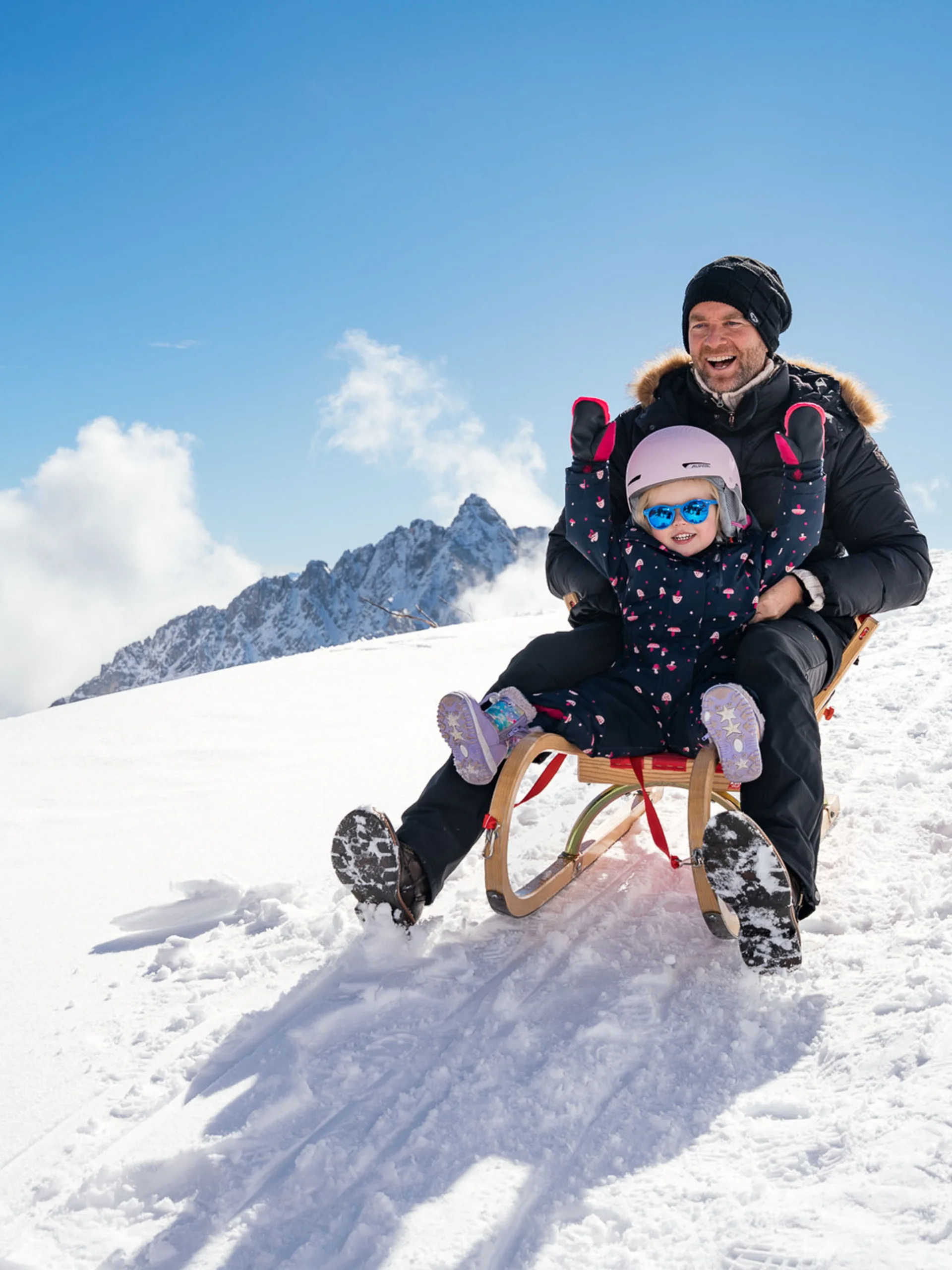 Vater und Kind rodeln glücklich im Schnee auf einem sonnigen Berg