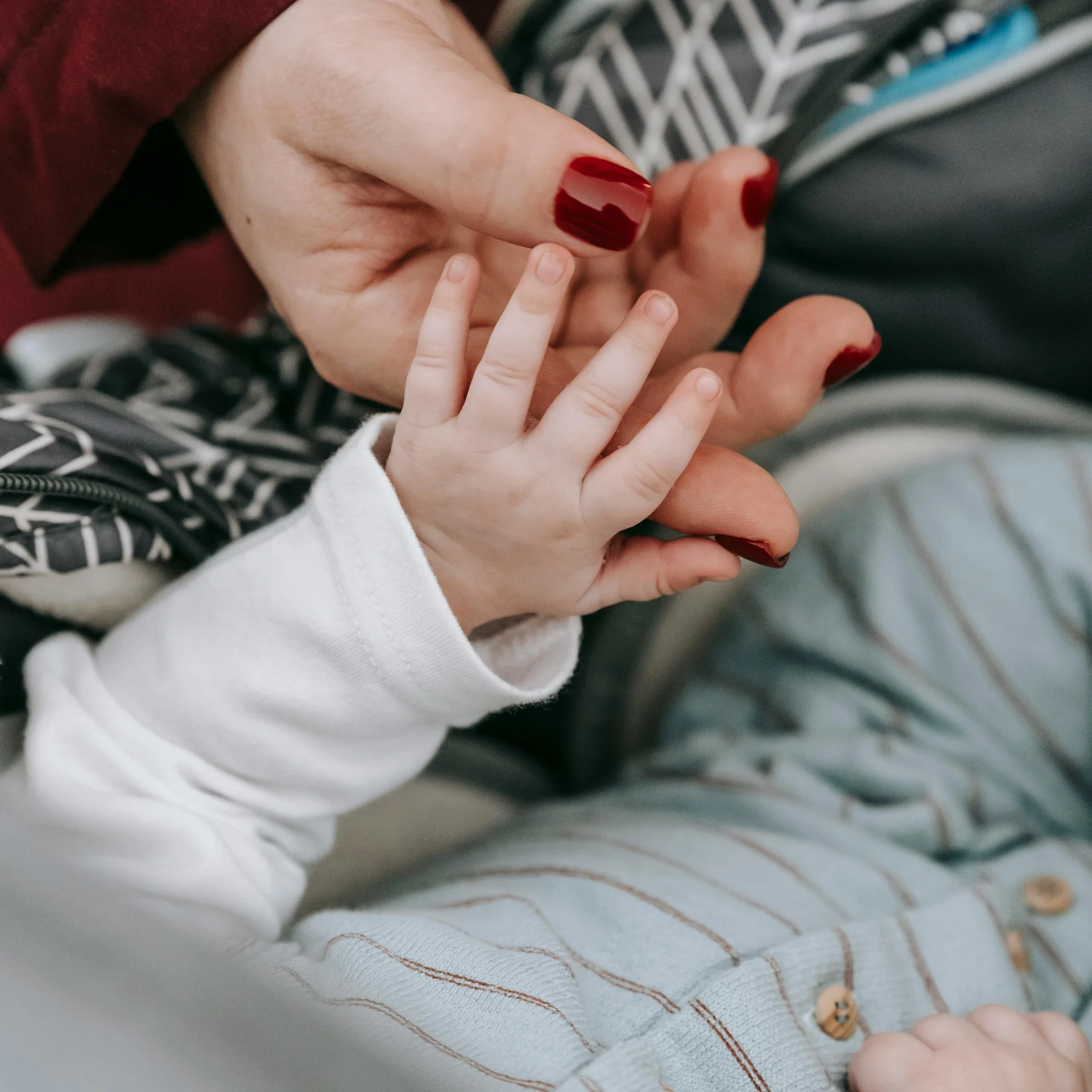 Adult hand with red nail polish holding baby's hand