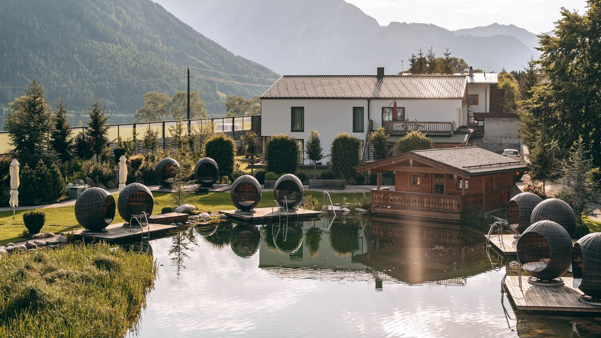 Haus und Holzpavillon am Teich mit Sitzkugeln und Bergblick