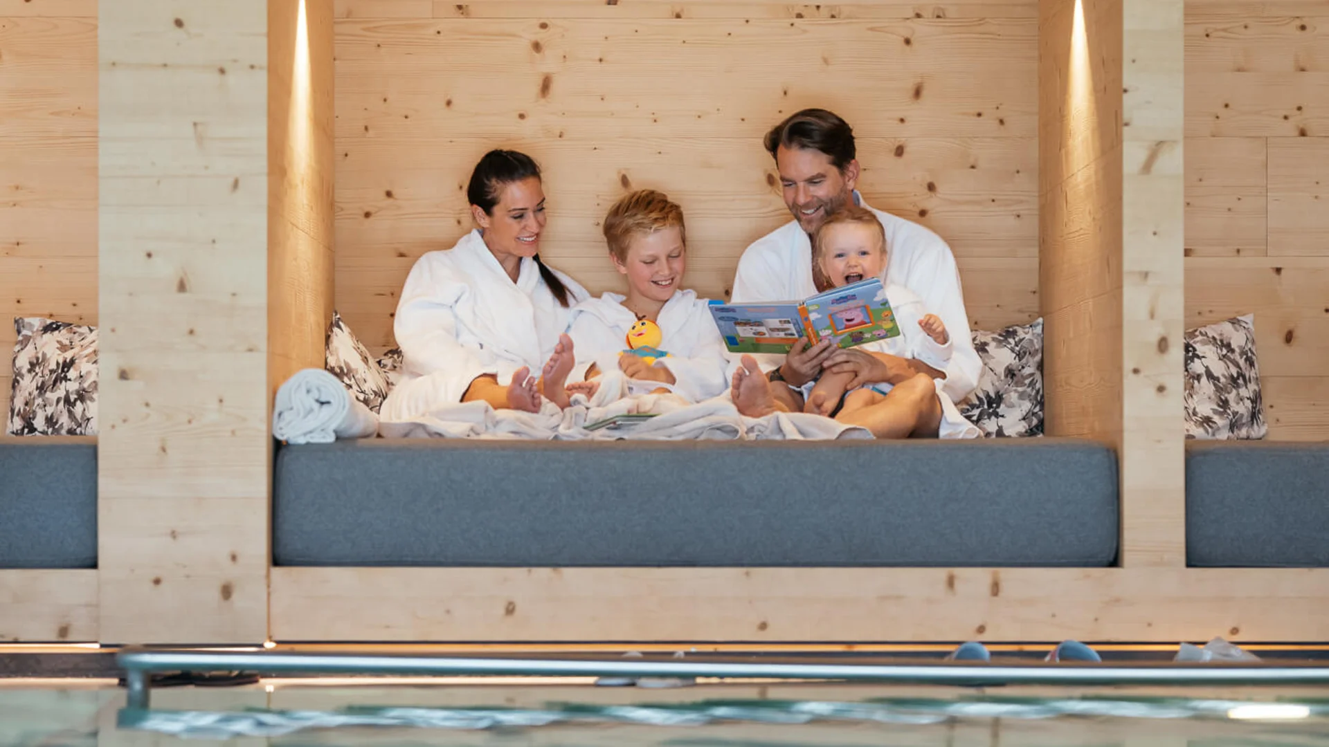 Familie in Bademänteln sitzt gemütlich an einem Holzruheraum neben dem Pool