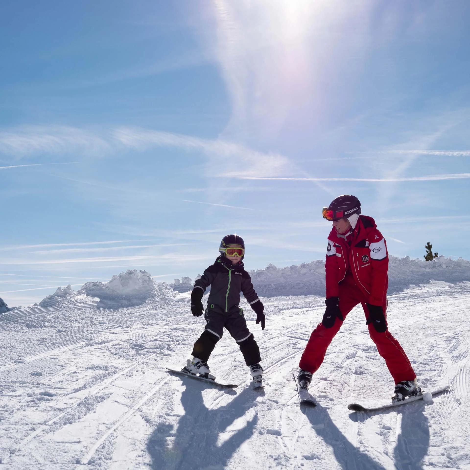 Child and ski instructor skiing on snow-covered slope under sunny sky