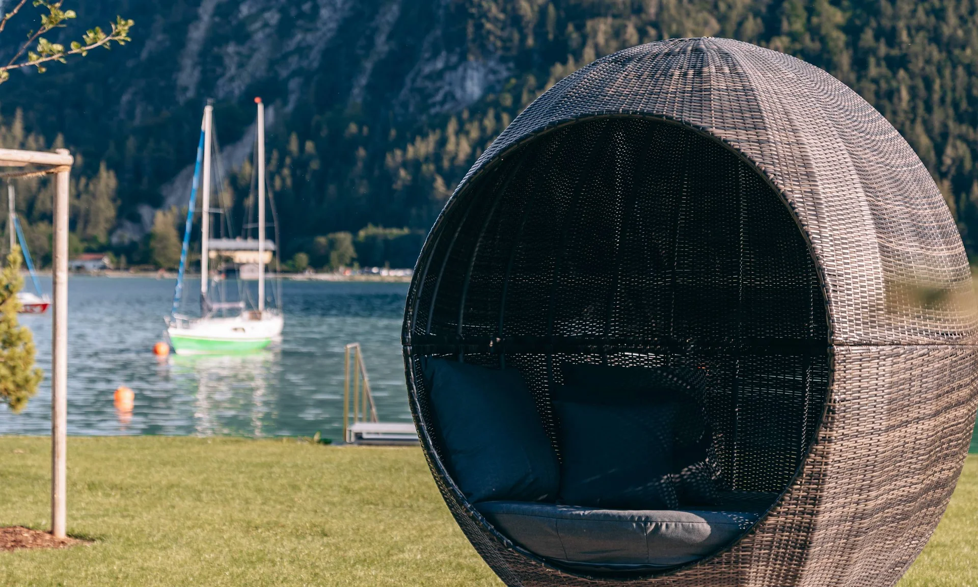 Rundes Gartenmöbel mit Kissen am See vor Bergkulisse