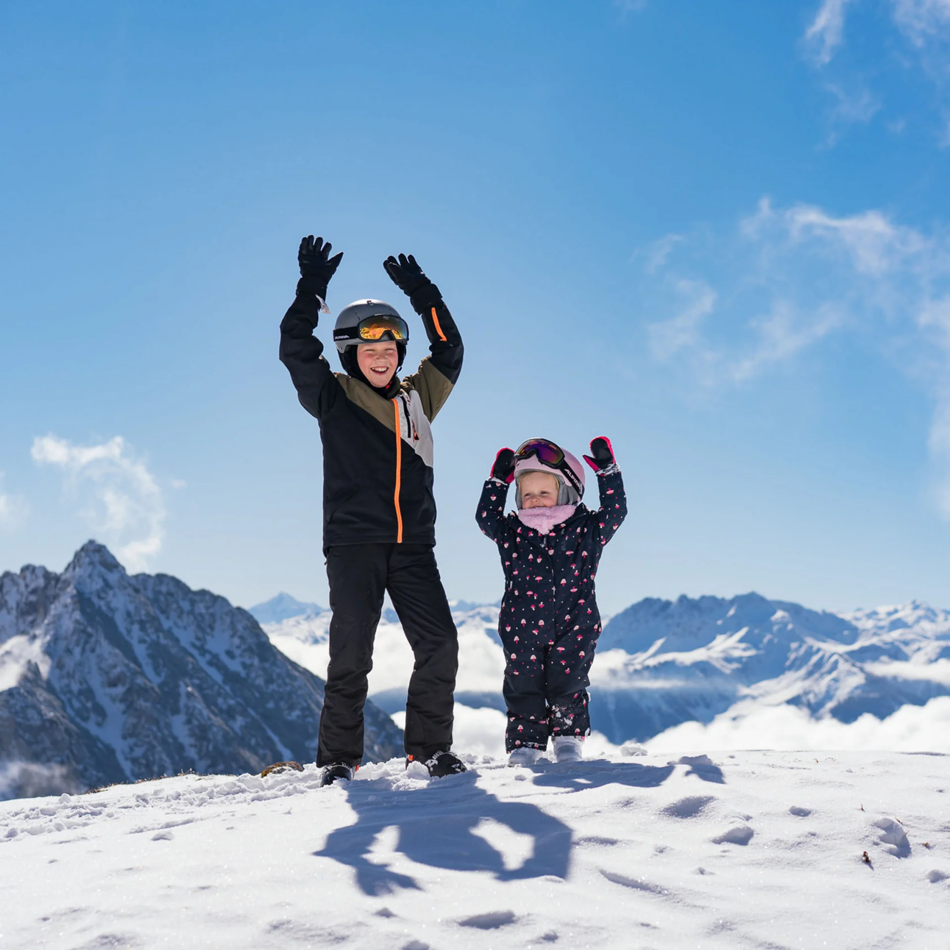 Familienzeit im Kinderhotel Buchau am Achensee Zwei Kinder in Skianzügen stehen im Schnee auf einem Berg mit erhobenen Armen