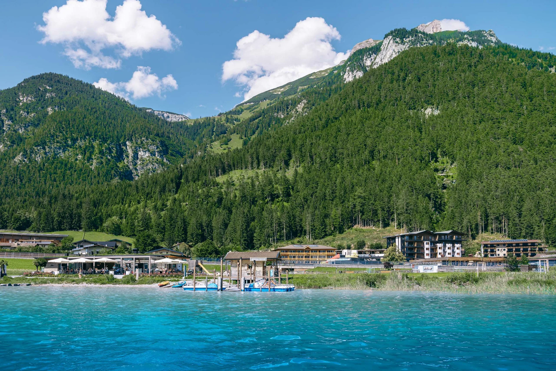 Klares blaues Wasser mit Bergkulisse und Gebäude am Ufer bei sonnigem Wetter
