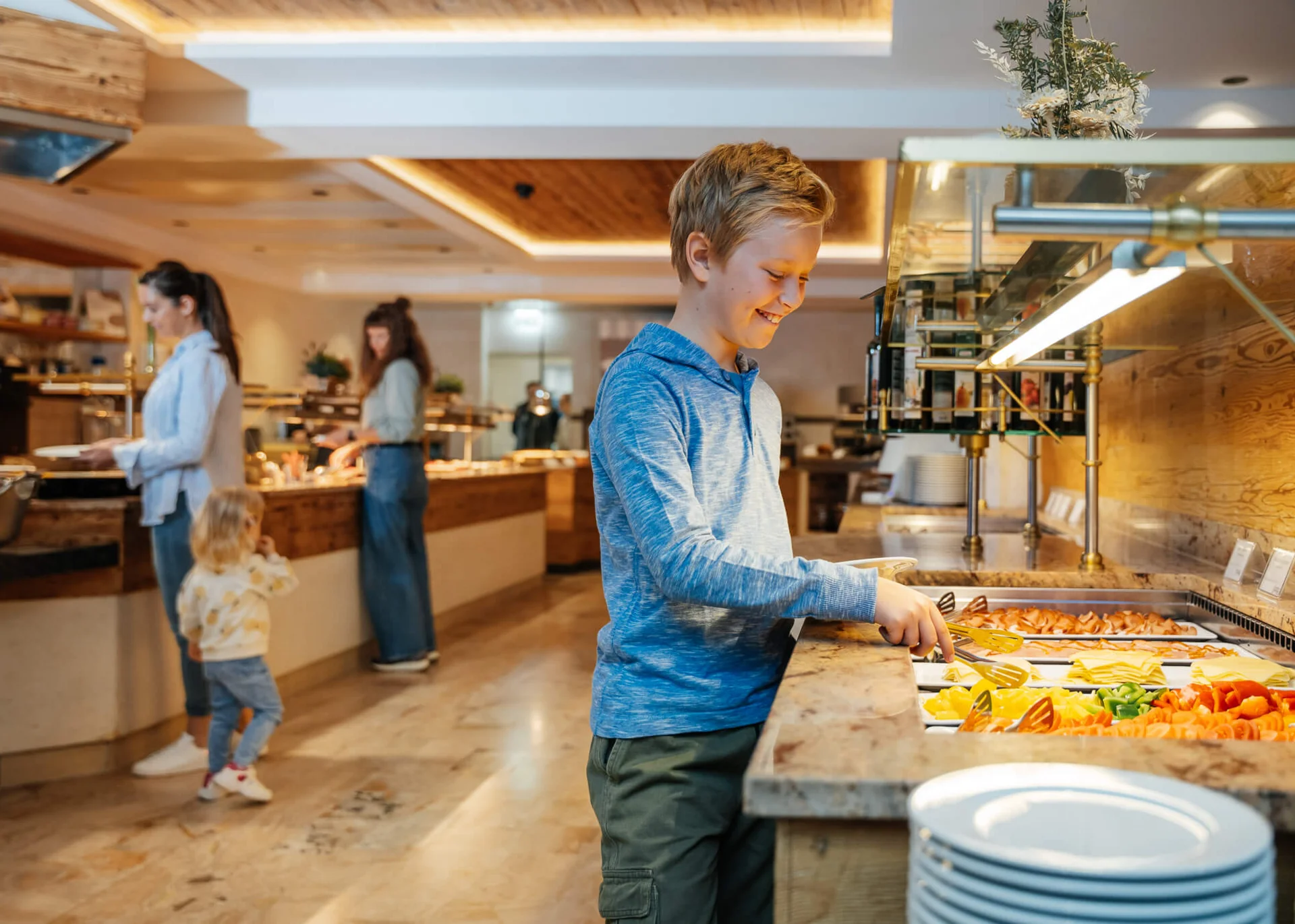 Junge nimmt Essen vom Buffet in einem Restaurant mit Familien im Hintergrund