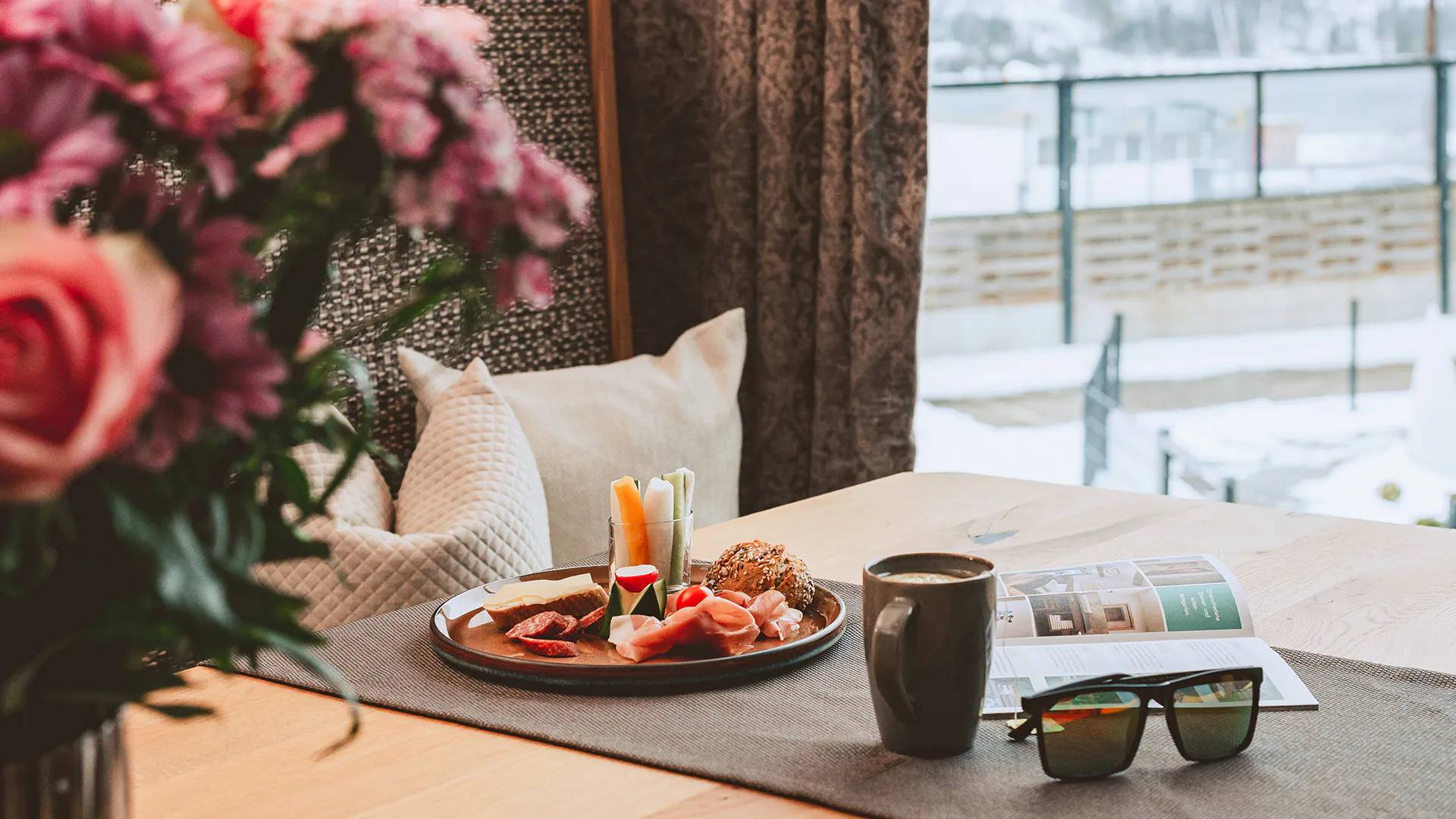 Frühstück mit Wurst, Käse, Gemüse, Kaffee und Buch auf Tisch mit Blumen
