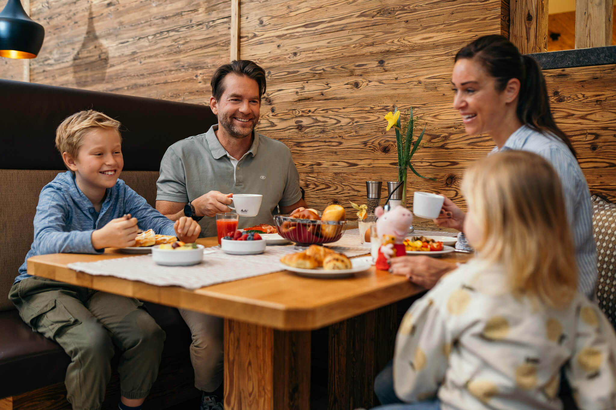 Familie mit zwei Kindern isst Frühstück an Holztisch in gemütlichem Restaurant
