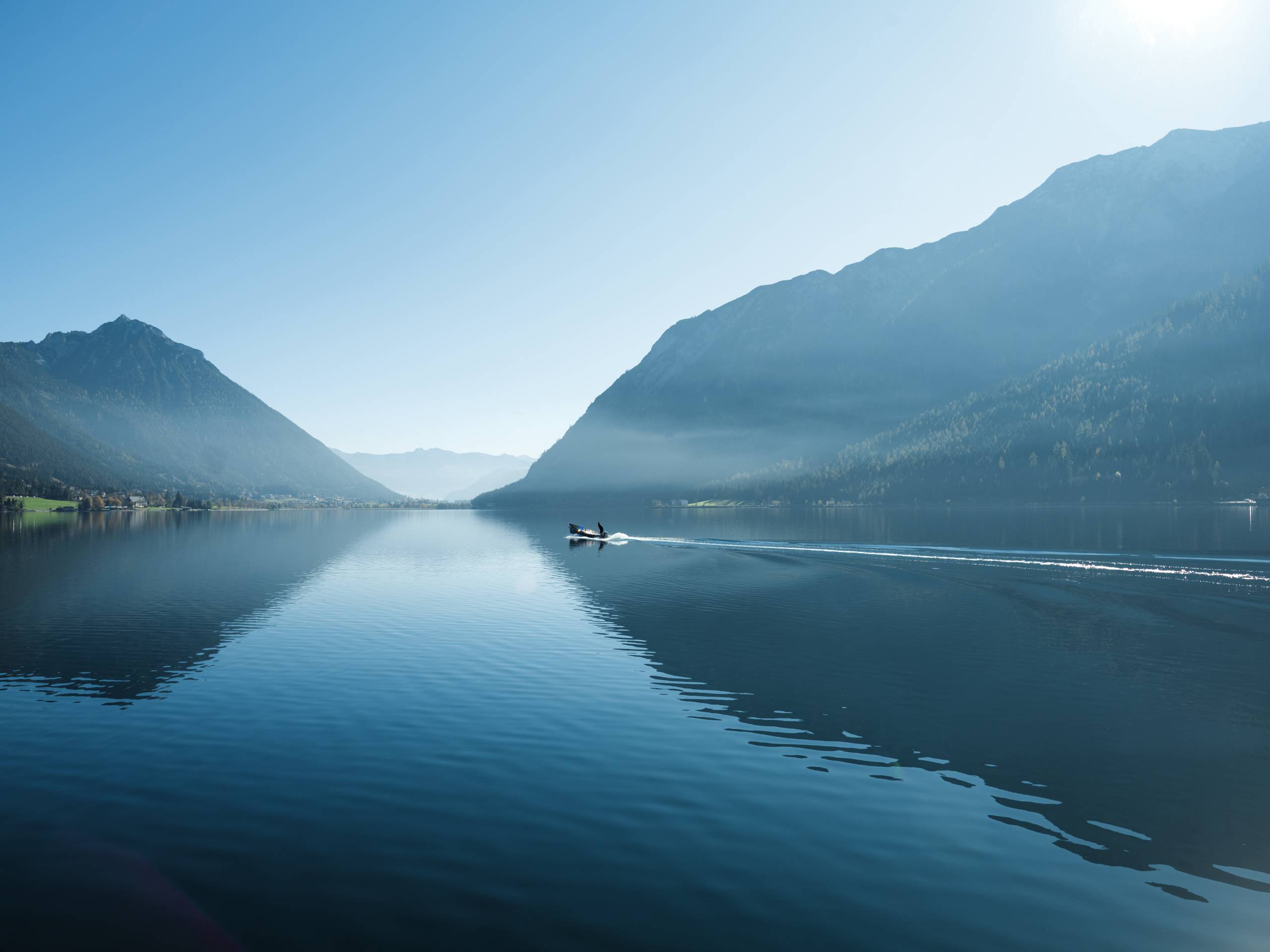 Boot fährt auf ruhigem See zwischen Bergen an klar blauem Himmel