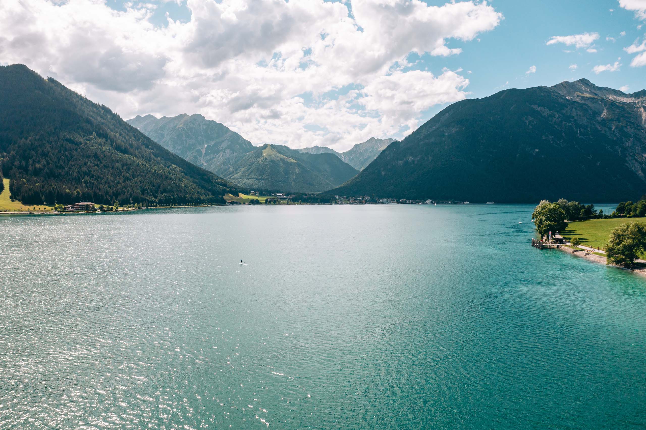 Blauer Bergsee umgeben von bewaldeten Bergen unter bewölktem Himmel